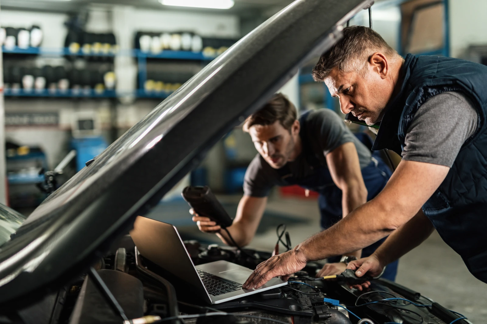 Auto mechanics using a laptop for car diagnostics while cooperating in a repair shop