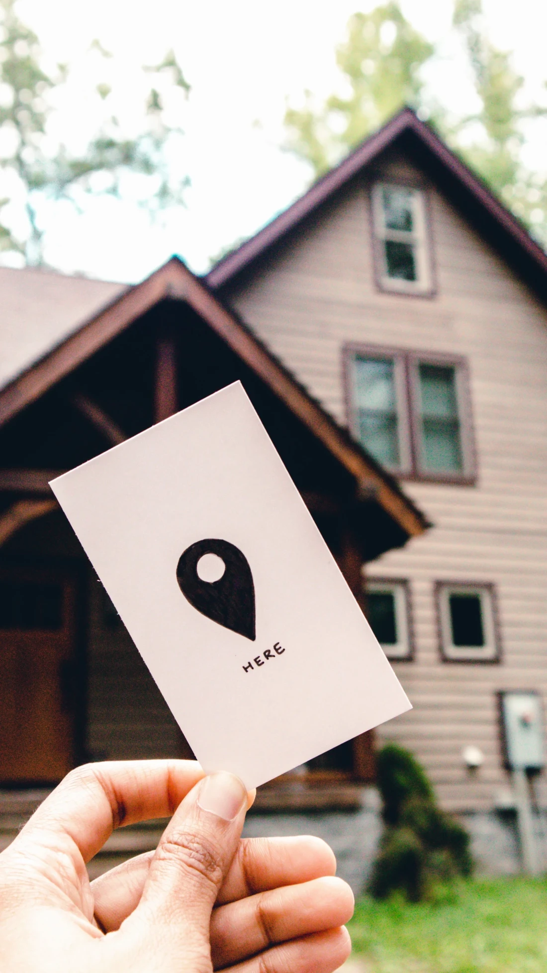 Hand holding a location pin card in front of a house